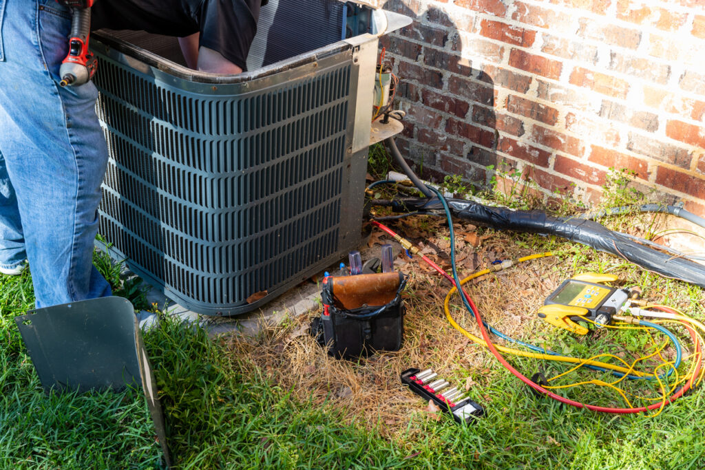 HVAC technician inspecting a repairing an AC system outside of a brick home.