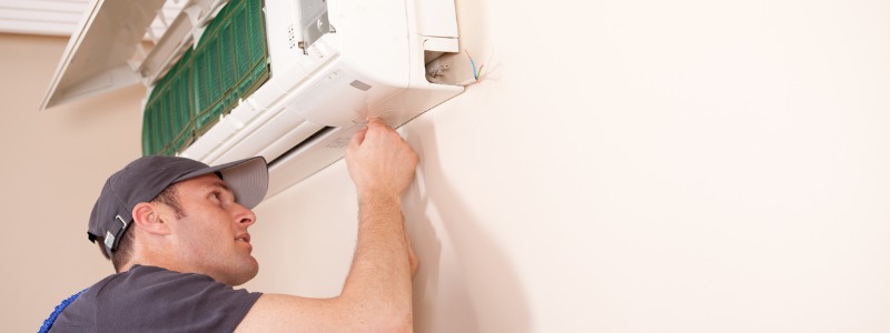 HVAC technician tuning up a ductless mini-split system on a white wall.
