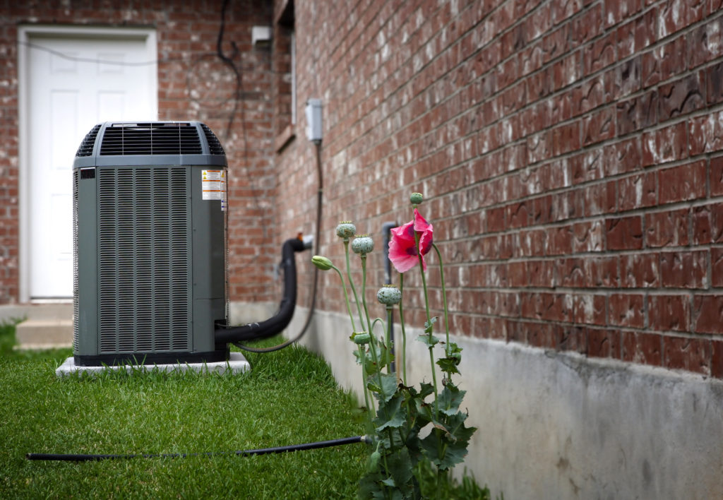 Outdoor HVAC system next to bring house and spring flowers.