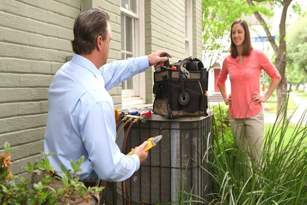 Young female homeowner talking to technician in yard while he repairs leaking AC unit.